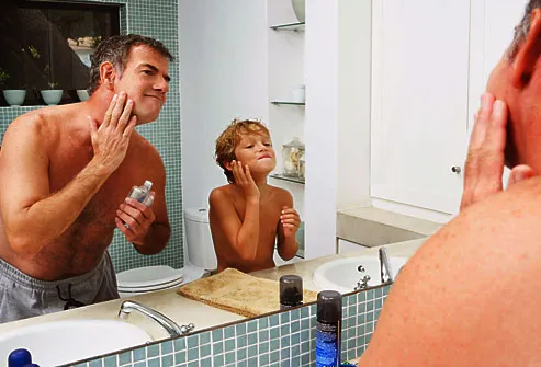 Father and son applying aftershave in mirror