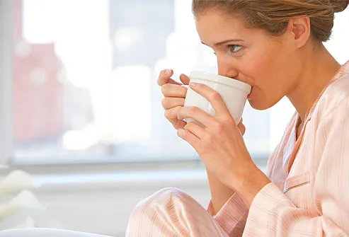 Young woman wearing pajamas, drinking coffee 
