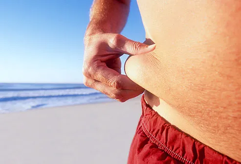 Man pinching fat on waist , beach in background