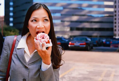Businesswoman standing outdoors, eating donut