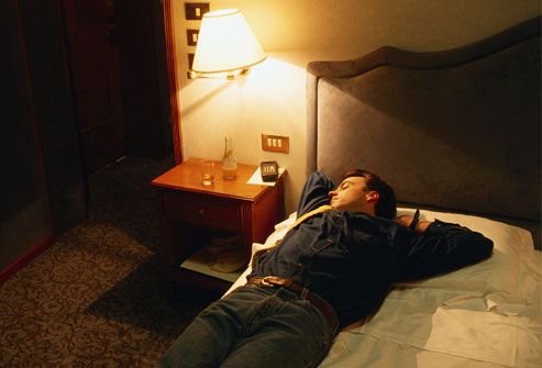 Man asleep on bed with light on, fully clothed