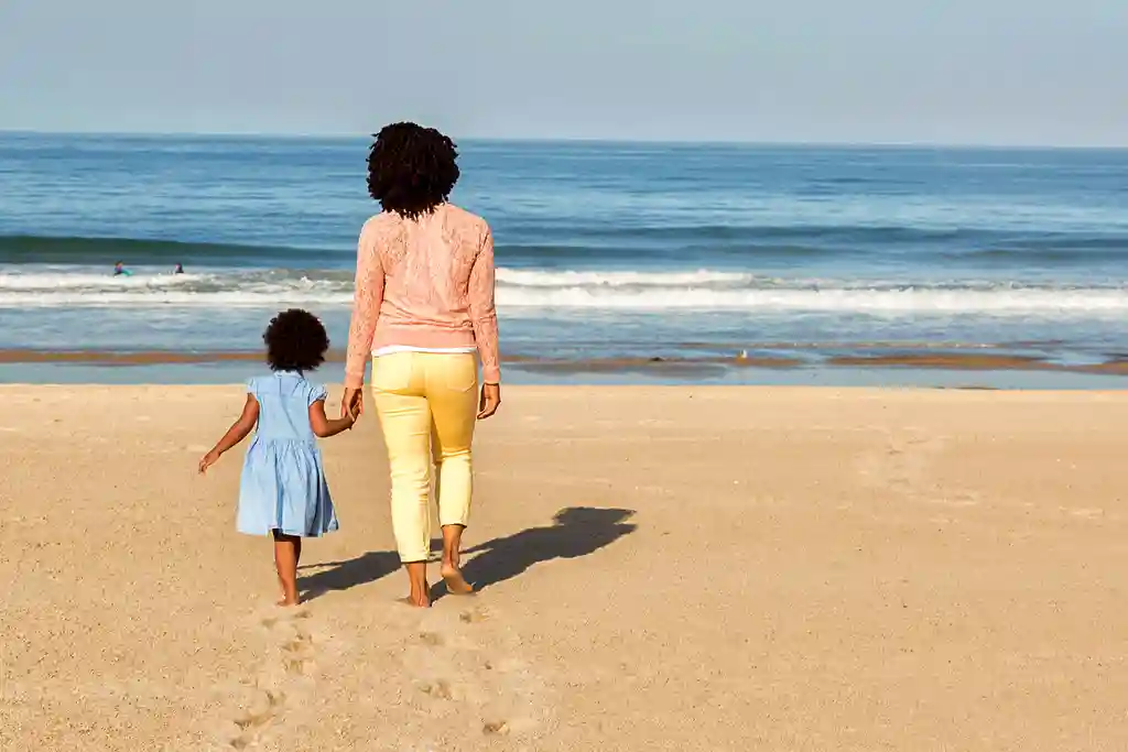 photo of mother and daughter walking on beach
