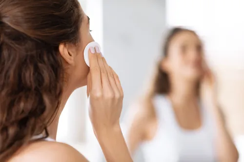 photo of woman using cotton pad looking at mirror