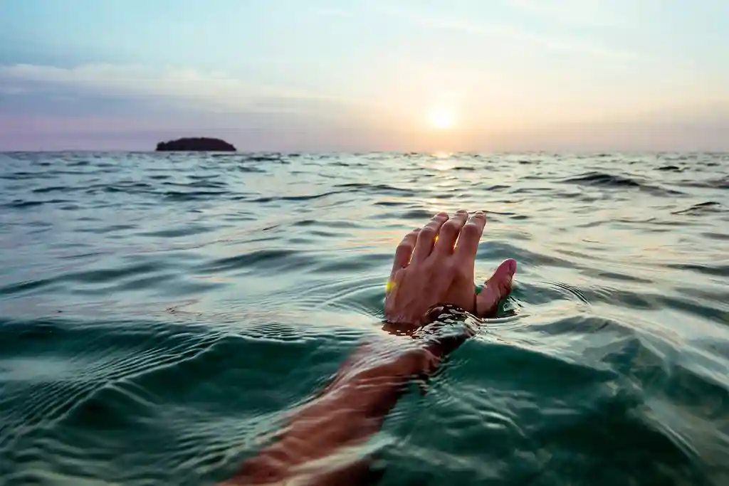 photo of swimmer hand rising from ocean at sunset