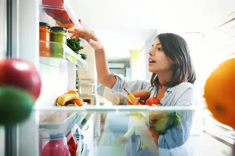 woman adding fruits and veg to refrigerator