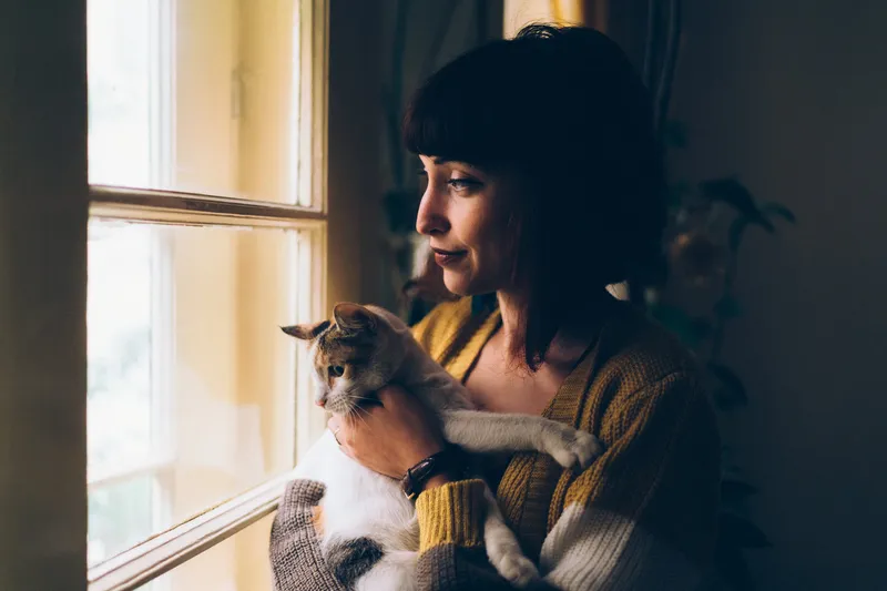 woman with a cat looks out window
