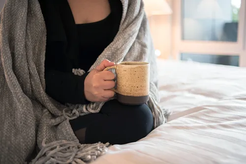 photo of person wrapped in blanket holding mug