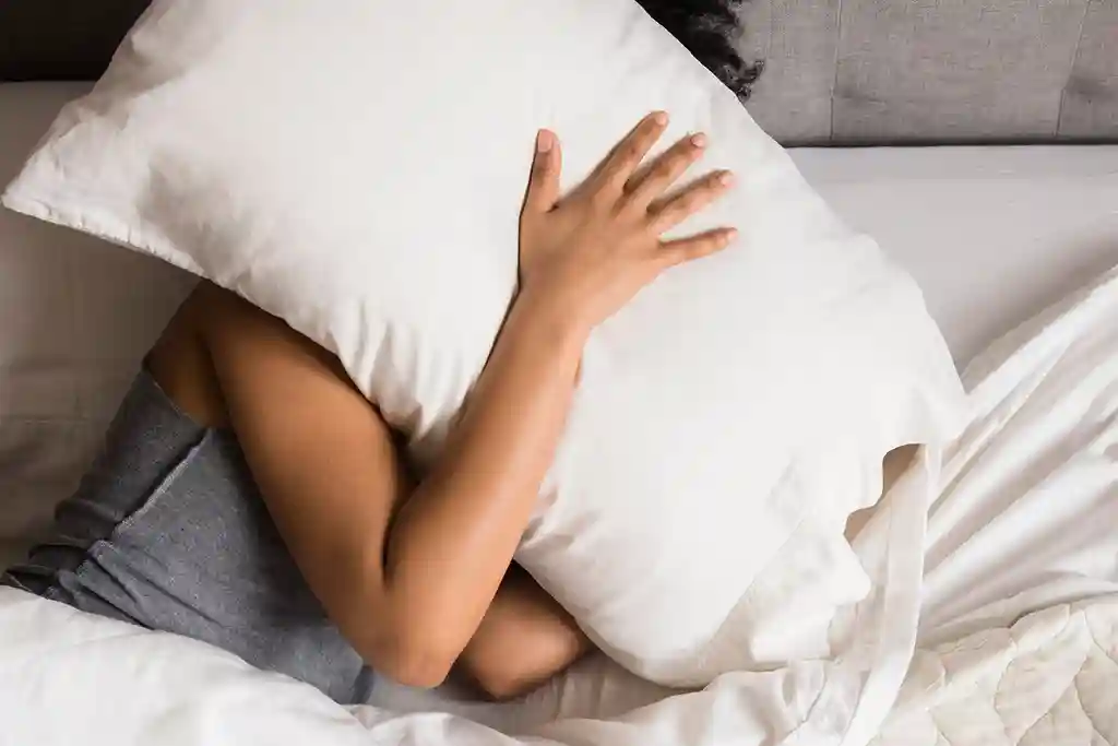 photo of woman on bed hiding face under pillow