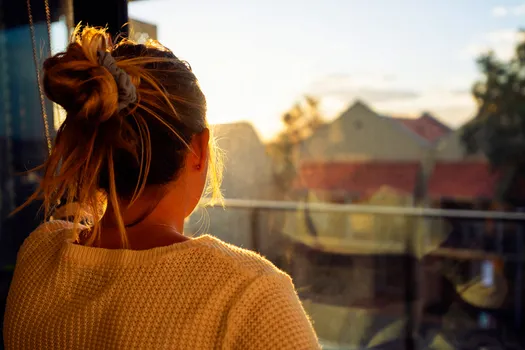 photo of woman looking through window at sunse