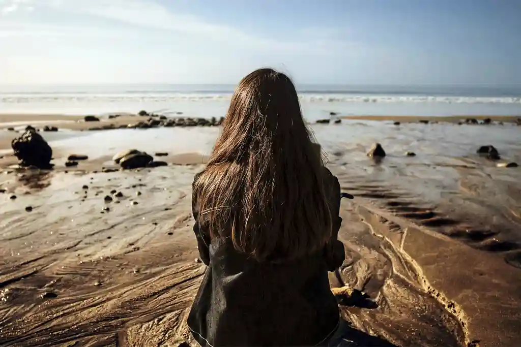 photo of woman sitting on sand looking at sea