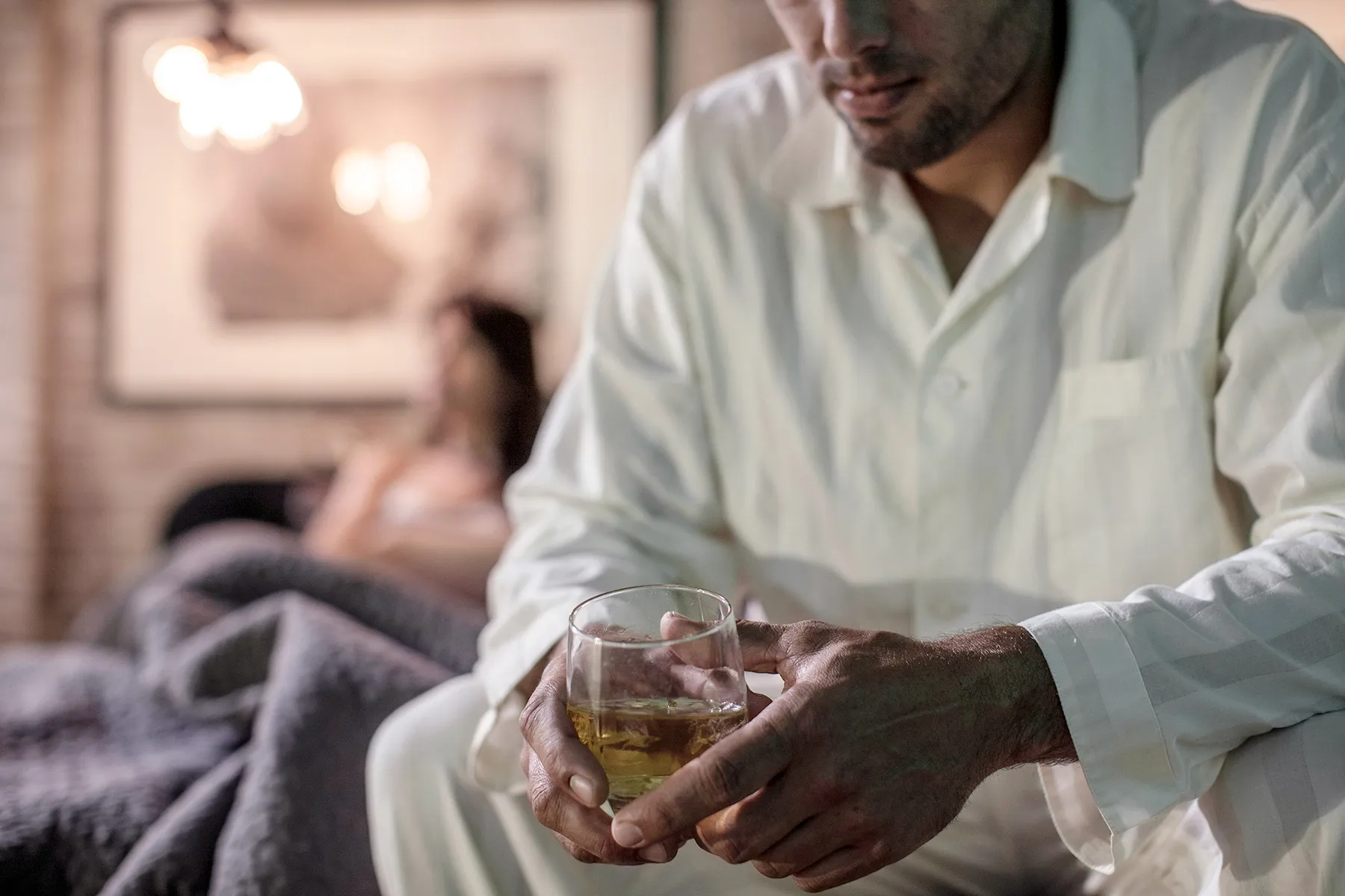 photo of man sitting on bed holding whiskey