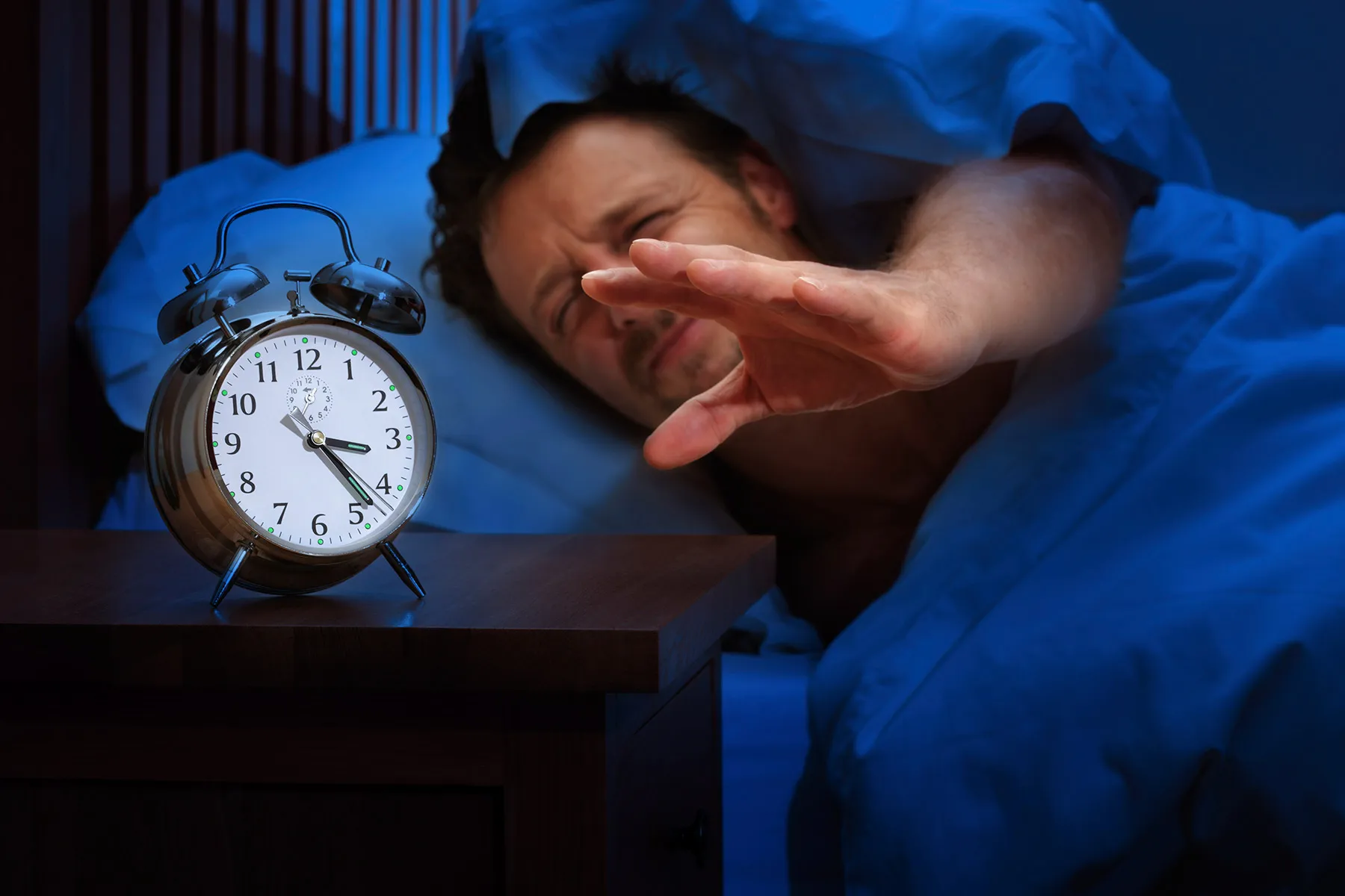 man reaching for alarm clock