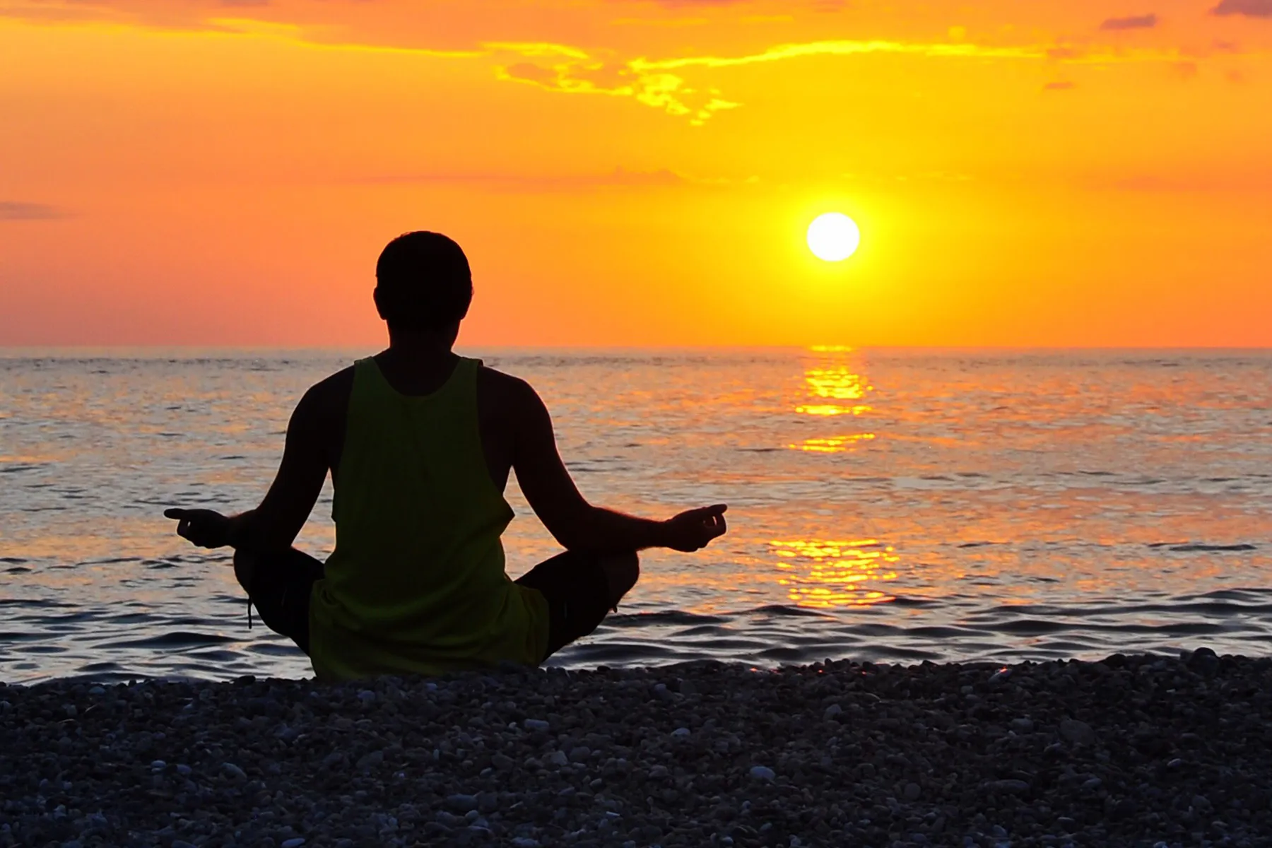 photo of man meditating by ocean at sunrise