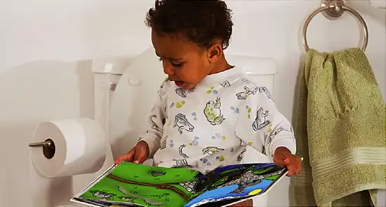 Little boy reading book while on the toilet