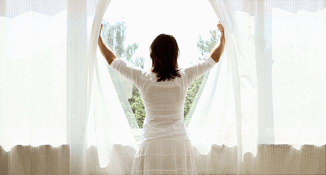 Woman opening curtains, looking out window
