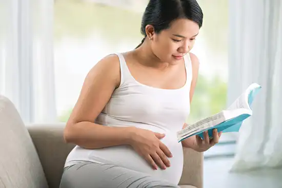 photo of pregnant woman reading book on sofa