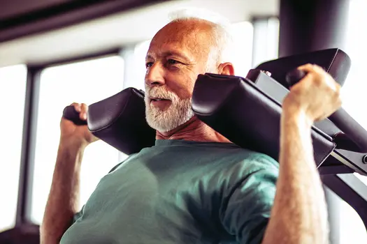 photo of senior man doing shoulder press in gym