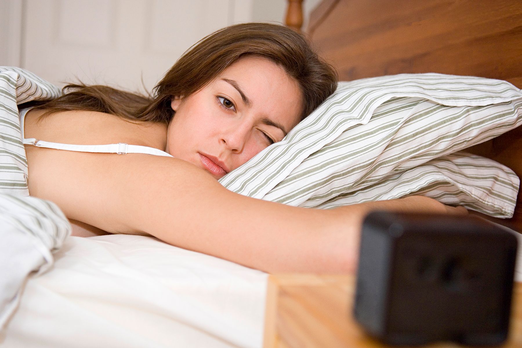 photo of sleepy woman in bed looking at clock