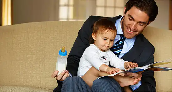father reading to daughter (15-18 months) on sofa,