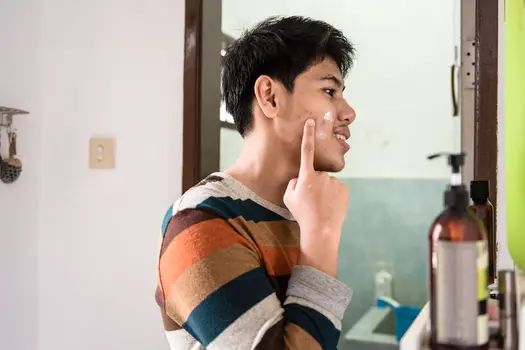 photo of young man applying acne cream to face