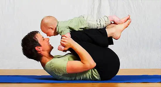 Mother in yoga pose balancing baby on her knees