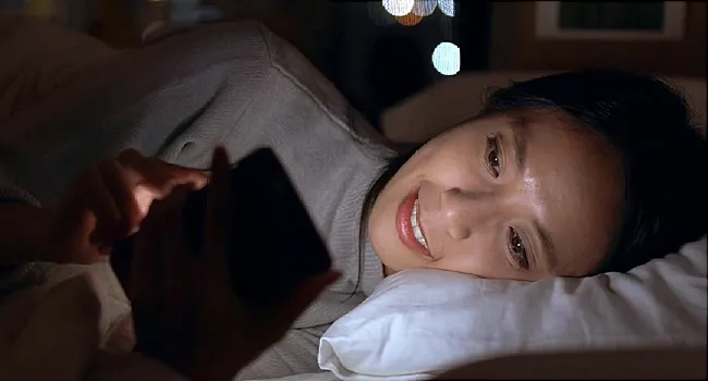 photo of woman using cell phone in bed