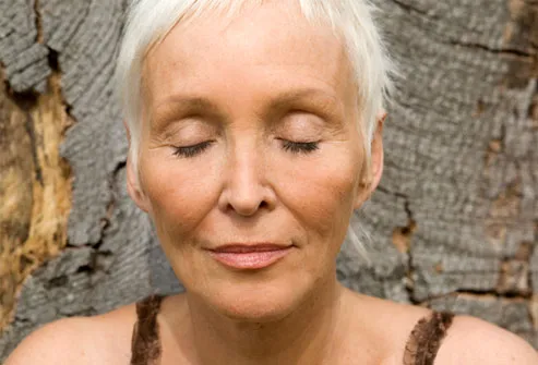 Mature woman with eyes closed leaning against tree