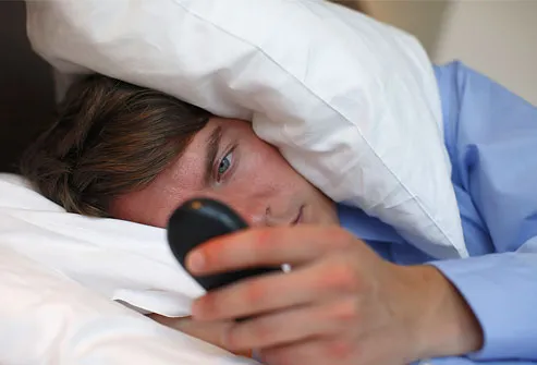 Young business man in bed, looking at mobile phone