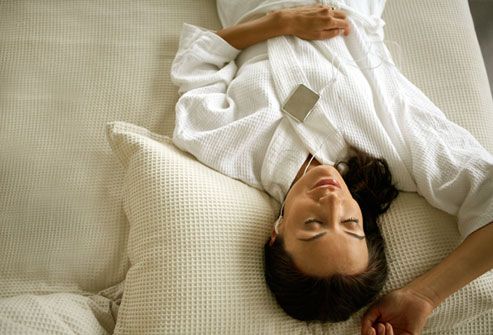 Woman wearing headphones while relaxing on bed