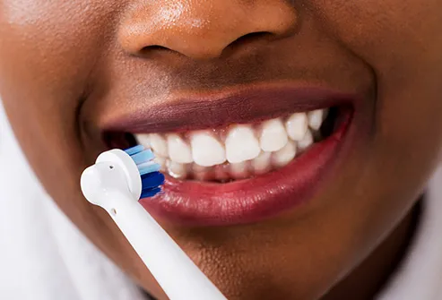 woman brushing teeth with electric toothbrush