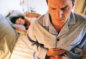 man on edge of bed with queasy stomach