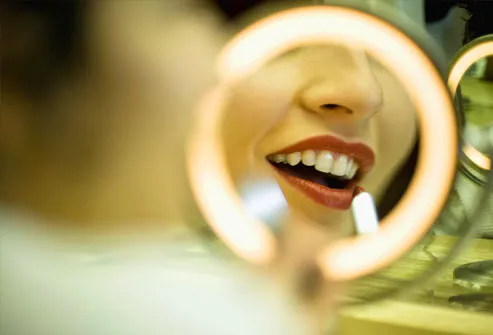 Woman applying lipstick in lit mirror