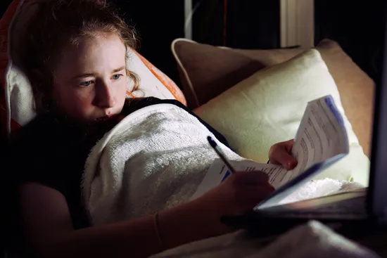 preteen studying in bed