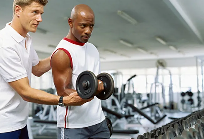 trainer helping man with free weights