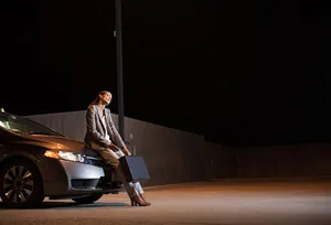 Fatigued woman leaning against car at night