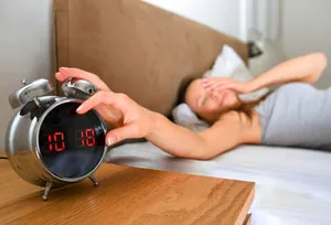 Woman silencing alarm clock late in the day