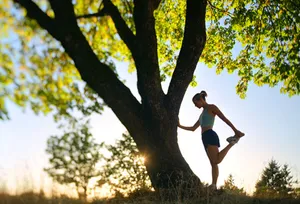 Woman jogger stretching against a tree at sunrise