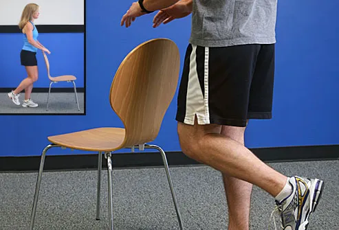 Trainer balancing on one leg near chair