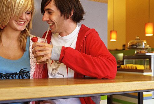 Young couple in cafe sharing drink through straws 