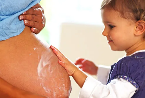 Girl applying lotion to pregnant mothers belly