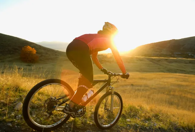 Woman riding mountain bike downhill at sunset