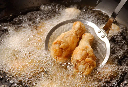 Chicken drumsticks emerging from vat of hot grease