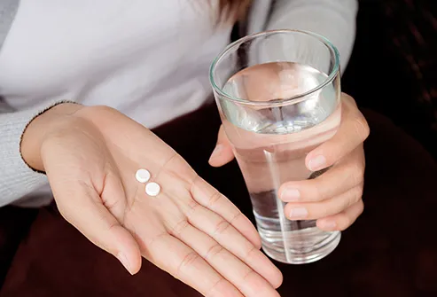hands holding aspirin and glass of water