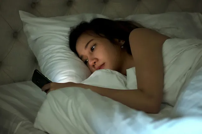 người phụ nữ sử dụng điện thoại thông minh trên giường