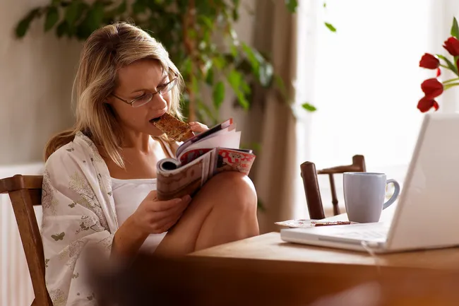 photo of woman reading magazine and eating