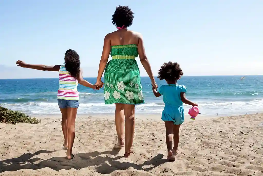 photo of woman and girls holding hands on beach