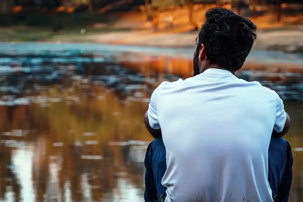 photo of young man sitting by lake