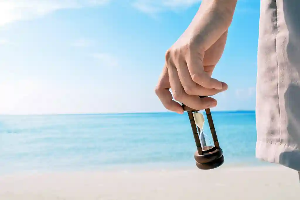 photo of hand holding hourglass at beach