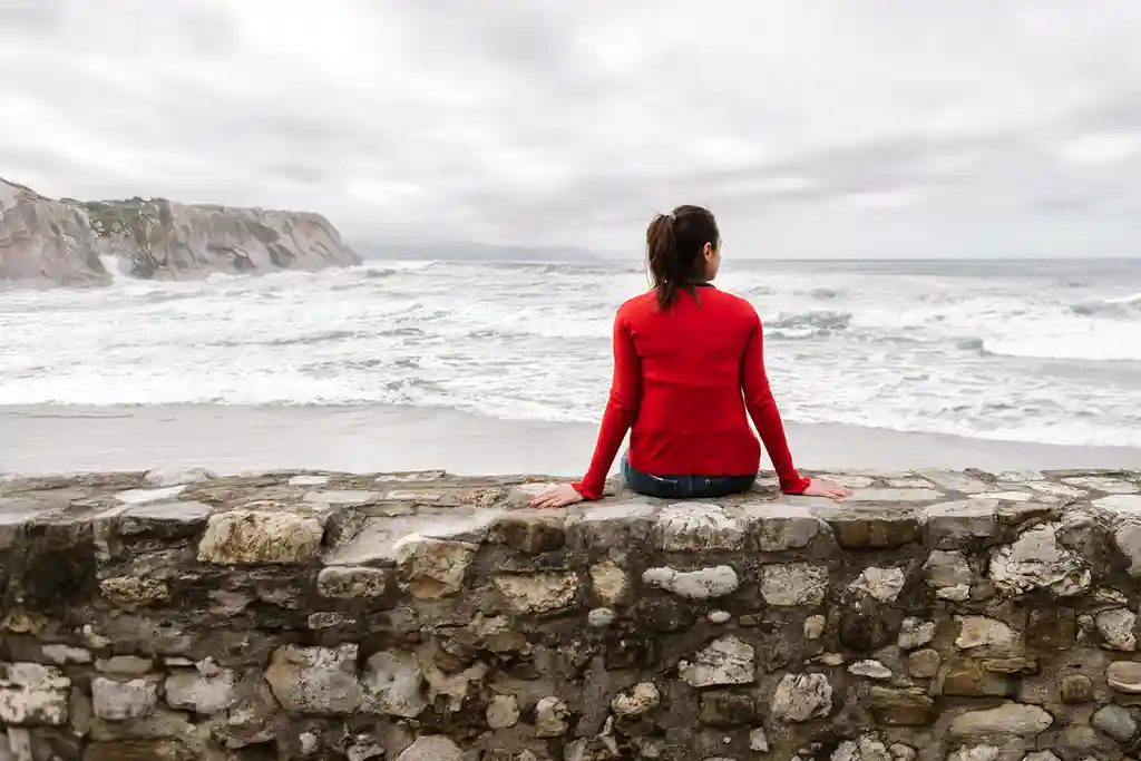 photo of woman resting on wall by ocean