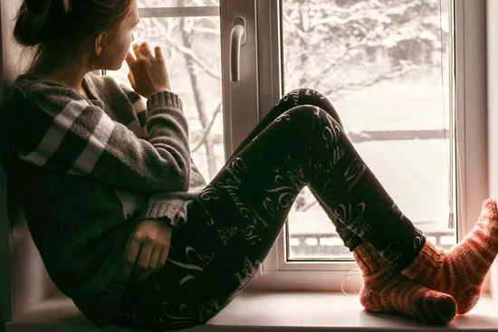 photo of woman sitting by window on winter day